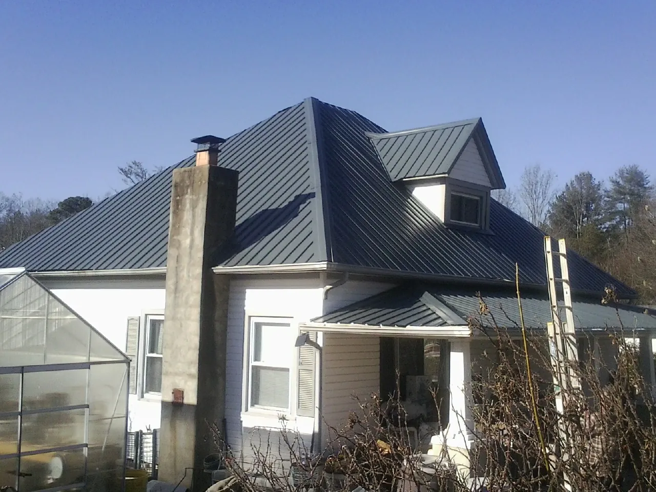 Dark blue standing seam metal roof on a white farmhouse with dormer — Slate & Tile Roof Repair by Roofing Brothers in Woodrow