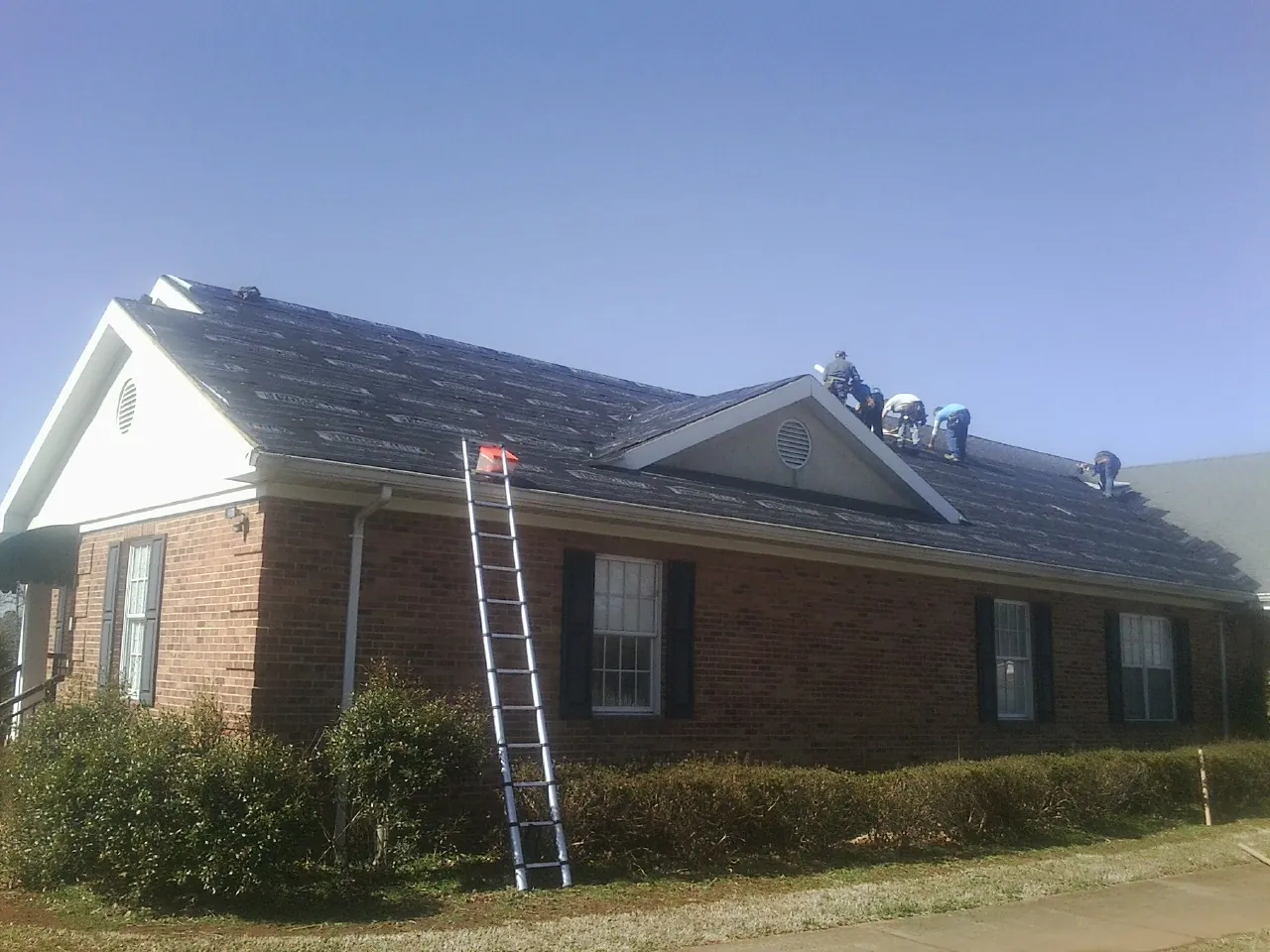 Crew tearing shingles off a brick ranch roof with a ladder set — Emergency Roof Repair work by our crew in Woodrow