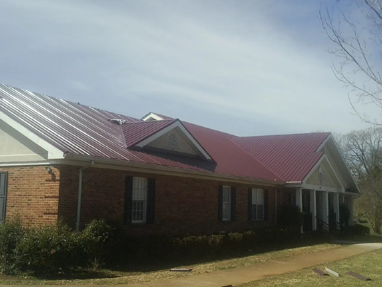 Red metal roof with gabled entries on a long brick building, from a Hail Damage Roof Repair job in Woodrow