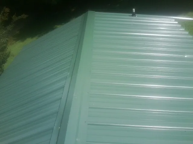 New green metal panels meeting at the ridge of a roof — Flat Roof Repair work by our crew in Woodrow
