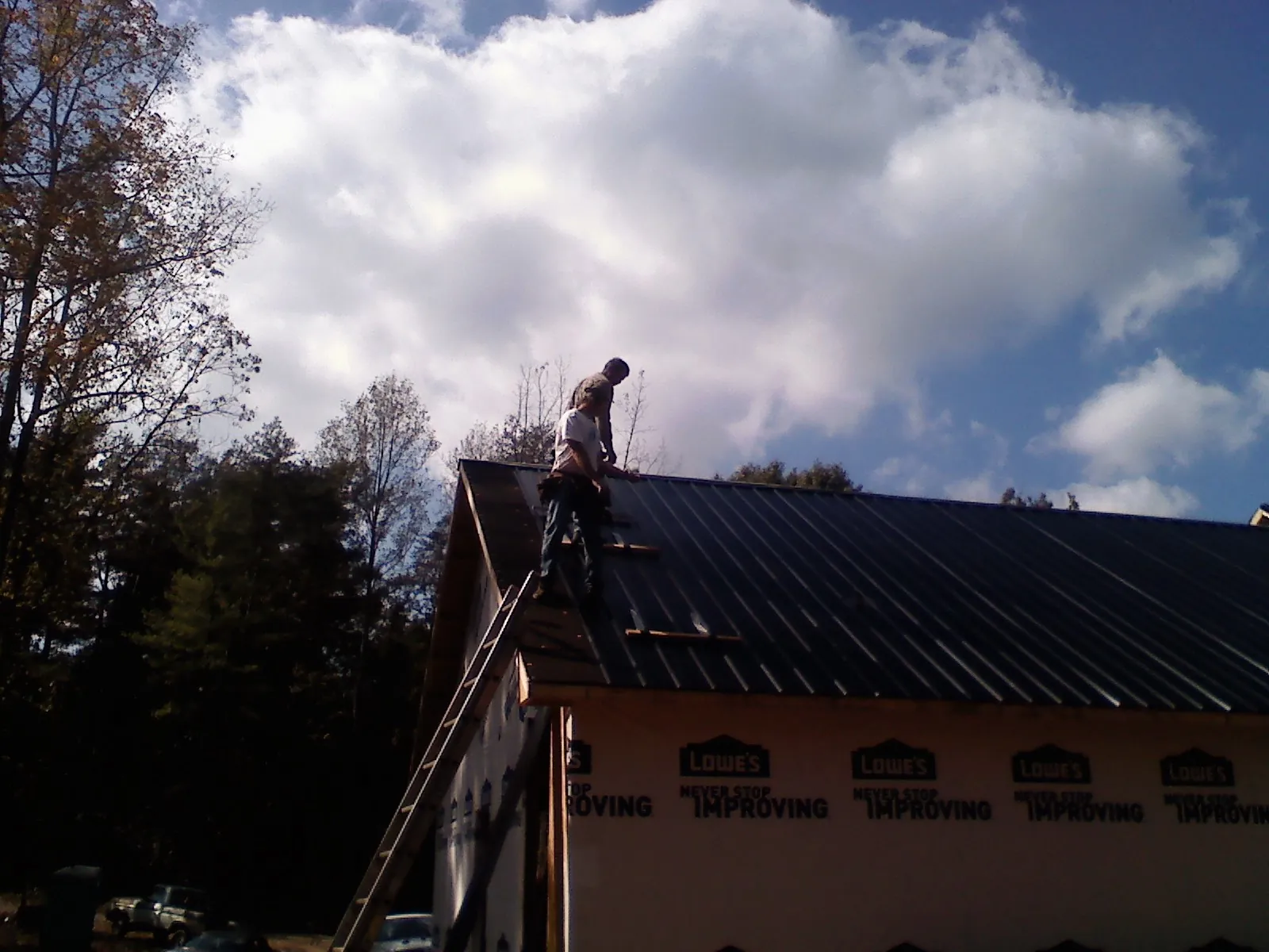 Roofer fastening dark metal panels high against a cloudy sky, from a Roof Inspection job in Woodrow