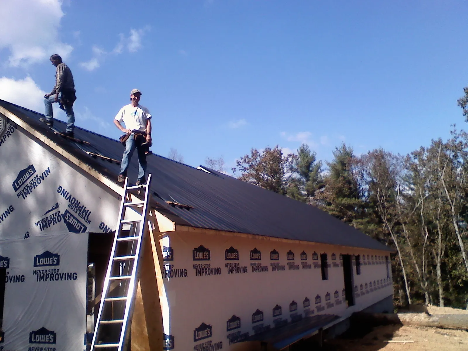 Two roofers standing on a long dark metal roof over a wrapped building in Woodrow