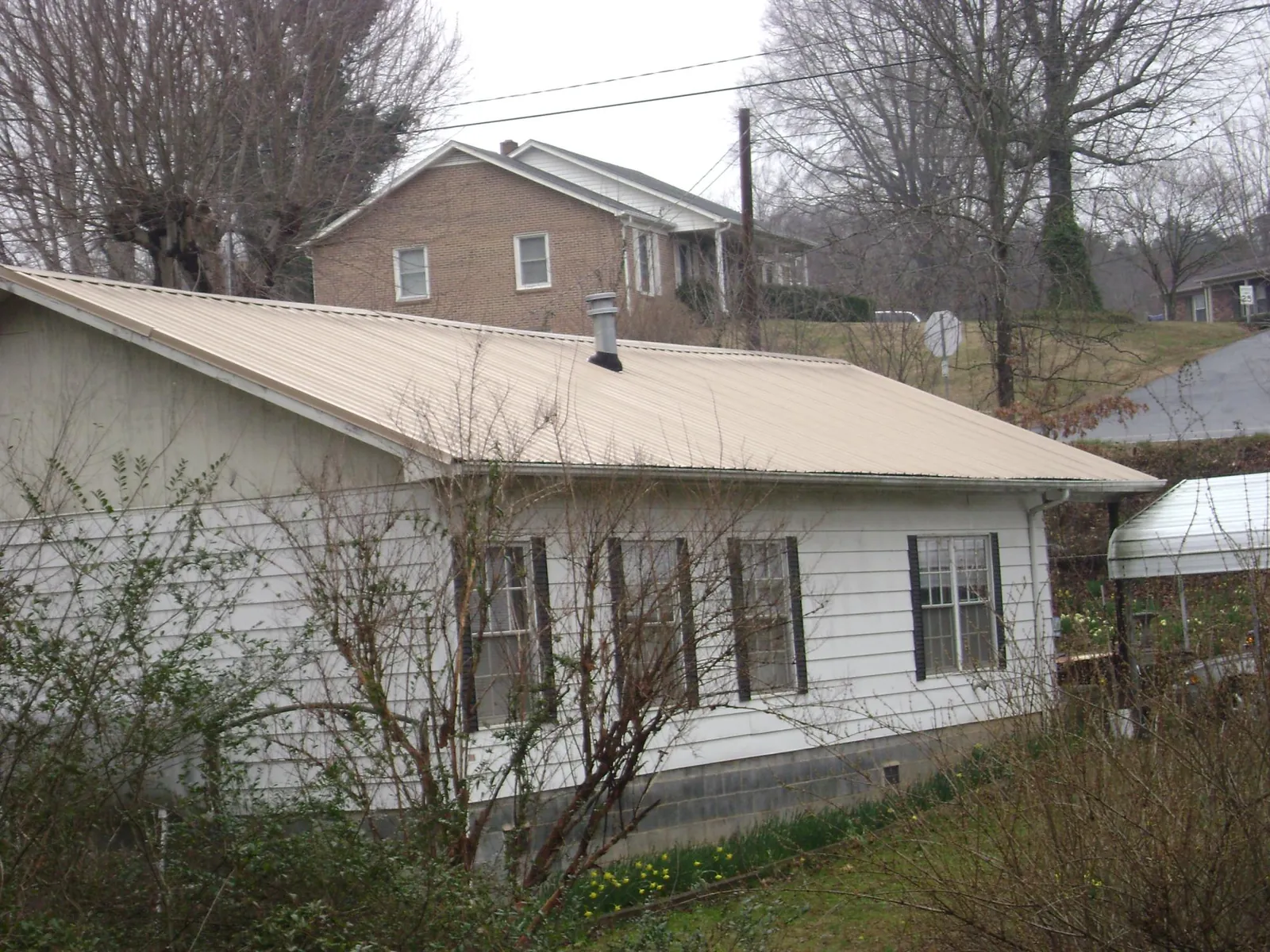 Tan metal roof on a white sided house set into a hillside — Commercial Roofing by Roofing Brothers in Woodrow