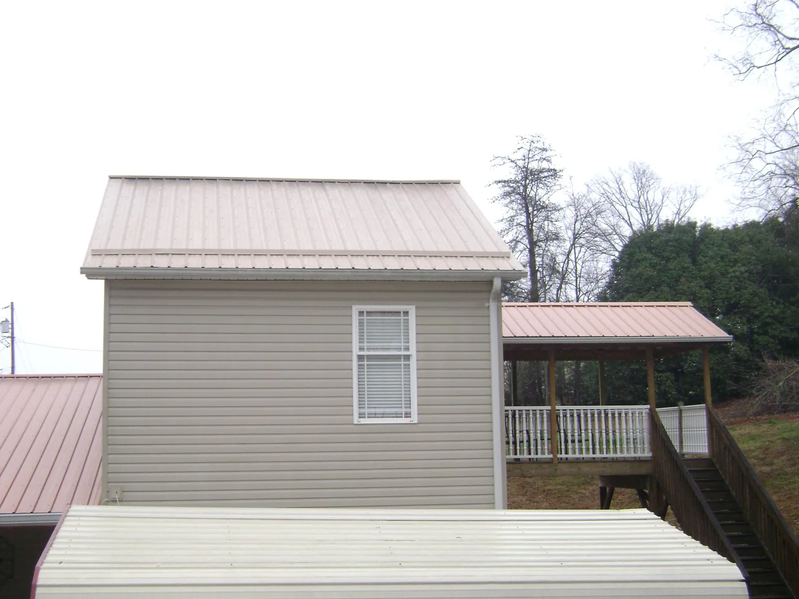 Tan metal roofs on a two story addition and attached porch, from a Roof Replacement job in Woodrow